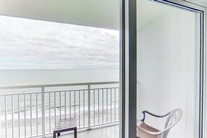 Un balcón con vista a la playa, barandilla de metal y un banco.