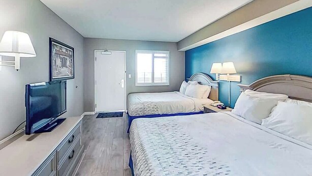 Una habitación de hotel con cama, mesita de noche, lámpara, televisión y ventana.