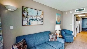Una sala de estar con un sofá azul, un cuadro de un puente, una lámpara y una silla.