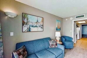 A living room with a blue sofa, a painting of a bridge, a lamp, and a chair.