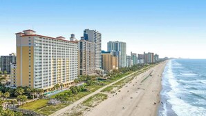 Un paisaje urbano costero con hoteles de gran altura, una playa arenosa y cielo despejado.