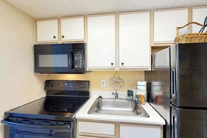 A compact kitchen with a microwave, stove, sink, and refrigerator. - Camelot by the Sea 1909 (Myrtle Beach)