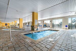 An indoor swimming pool with a tiled floor, lounge chairs, and a clear view of the sky through large windows. - Camelot by the Sea 1909 (Myrtle Beach)