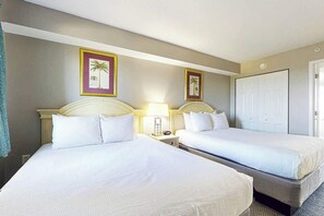 A hotel room with two beds, a nightstand with a lamp, and a door. - Camelot by the Sea 1711 (Myrtle Beach)