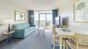 Ett hotellrum med en soffa, ett litet bord, en TV och en balkong med stolar.