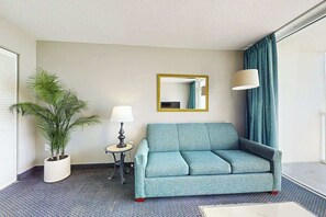 Ein Hotelzimmer mit einer Couch, einem kleinen Tisch mit Lampe, einer Topfpflanze und einem Spiegel an der Wand.