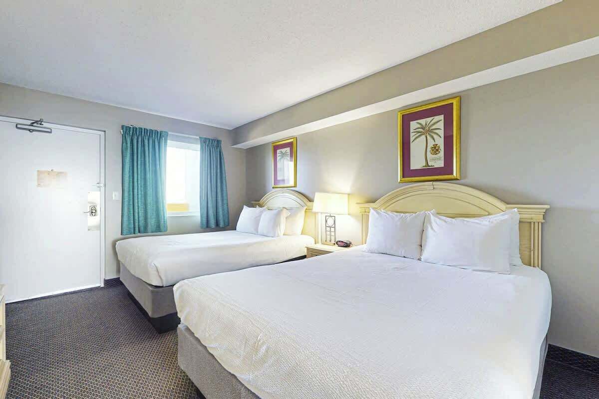 A hotel room with two beds, a door, a window with curtains, and two wall-mounted lamps.
