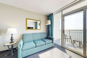 Ein Hotelzimmer mit Sofa, Tisch, Lampe, Spiegel und einem Balkon mit Blick.