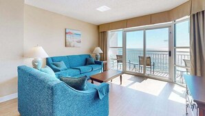 Quarto de hotel com varanda, sofá, mesa e um quadro na parede.
