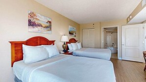 Quarto de hotel com duas camas, um quadro na parede e uma porta que dá para outro cômodo.