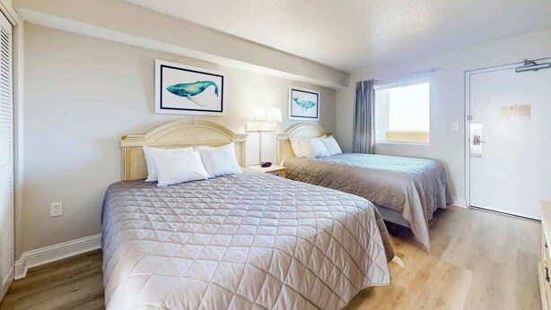 A hotel room with two beds, a door, and a window. - Camelot by the Sea 1704 (Myrtle Beach)