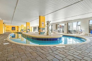 An indoor swimming pool with a tiled edge, a statue, and a brick floor. - Camelot by the Sea 1704 (Myrtle Beach)