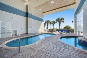 An indoor swimming pool area with two pools, a covered seating area, and a view of palm trees. - Carolinian Beach Resort 1232 (Myrtle Beach)