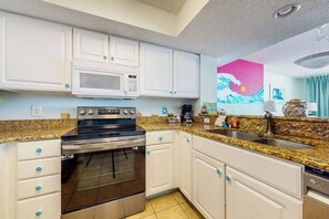 A kitchen with white cabinets, a stainless steel oven, a microwave, and a granite countertop. - Carolinian Beach Resort 1232 (Myrtle Beach)