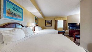 Quarto de hotel com duas camas, televisão e obras de arte nas paredes.