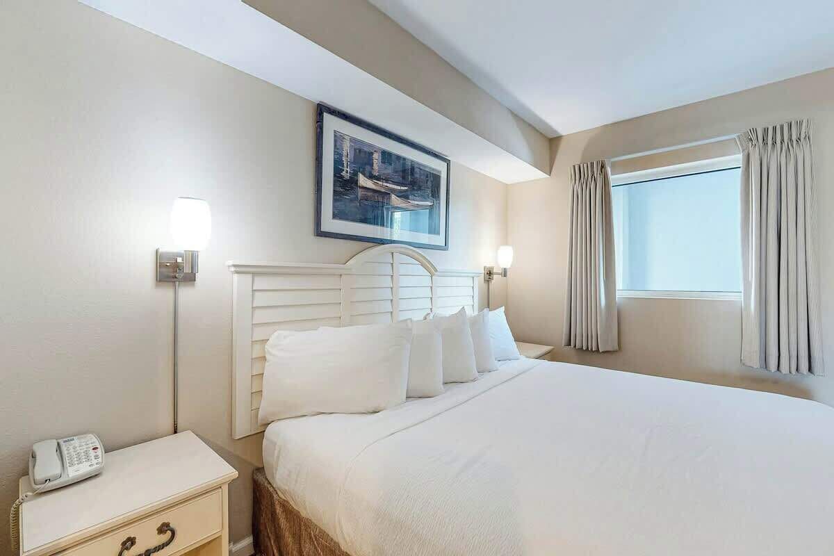 A hotel room with a large bed, a bedside table with a phone, and a window with curtains.