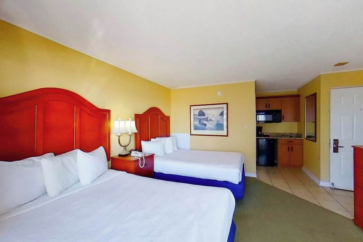 A hotel room with two beds, a small kitchenette, and a bathroom.