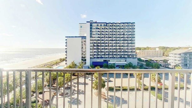 Un hôtel de grande hauteur doté de nombreux balcons, d’un parking et offrant une vue sur la plage.