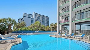 Une piscine avec des chaises longues, un bâtiment doté de balcons et des palmiers.