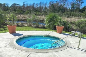 Ein runder Pool mit Metallleiter, umgeben von einer Betonplattform, mit zwei Terrakotta-Pflanzgefäßen und einer natürlichen Landschaft im Hintergrund.