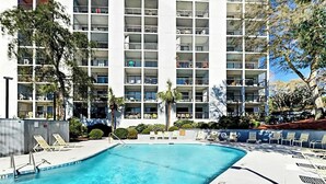 Une piscine avec des chaises longues et, en arrière-plan, un immeuble à plusieurs étages doté de balcons.