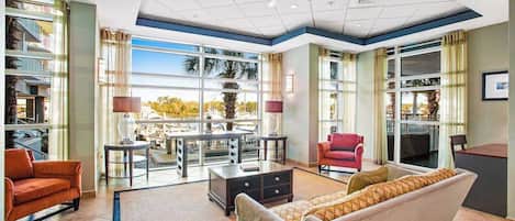 A spacious living area with a sofa, armchairs, and a coffee table. There are large windows providing a view of the outdoors.
