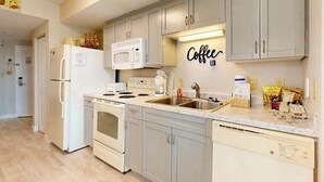 A modern kitchen with white appliances, a marble countertop, and a wall-mounted coffee sign. - Harbourgate Unit 0316 (North Myrtle Beach)