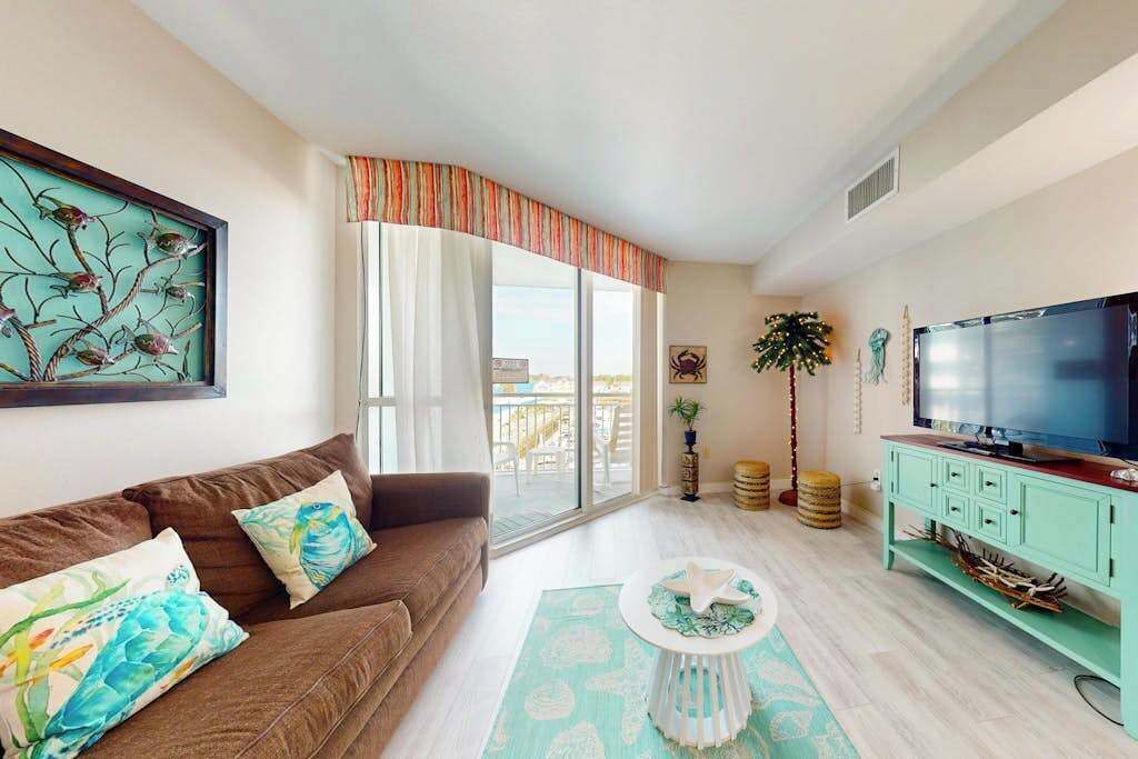 A living room with a sofa, a television, a coffee table, and a large window with curtains.