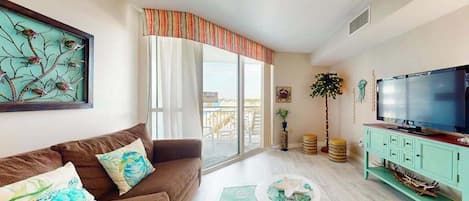 A living room with a sofa, a television, a coffee table, and a large window with curtains.