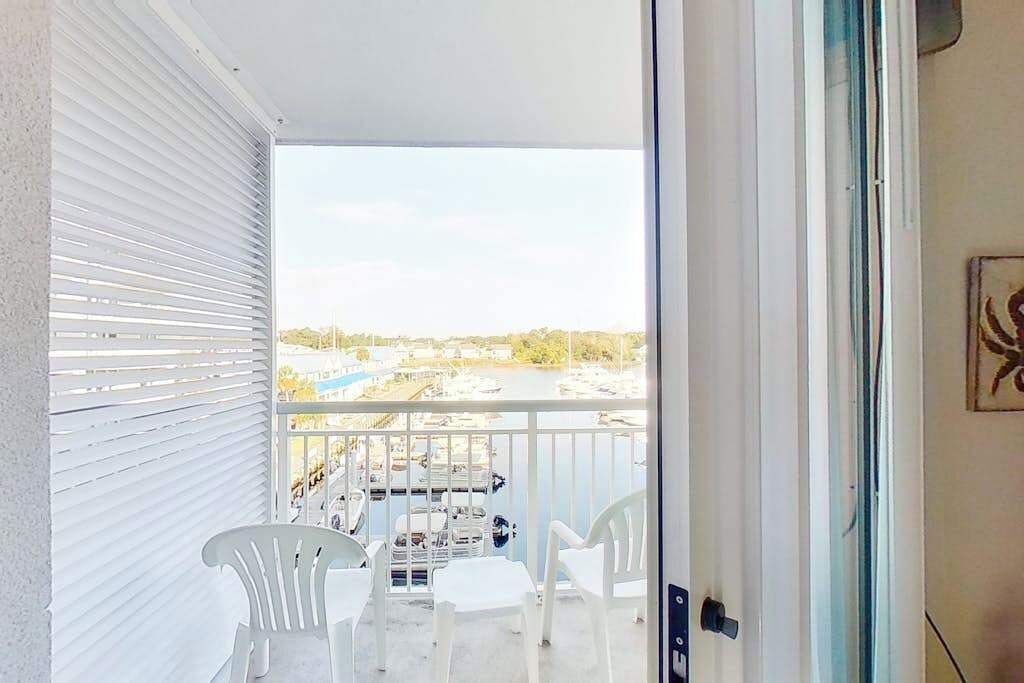 A balcony with white chairs, a table, and a view of a marina with boats.