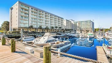 Un port de plaisance avec des bateaux amarrés, une jetée en bois et un bâtiment d’hôtel à plusieurs étages doté de balcons.