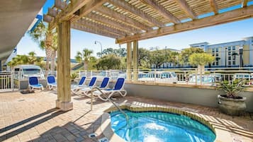 A pool area with lounge chairs and a hot tub, surrounded by a wooden pergola.