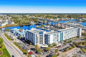 A multi-story hotel with a parking lot, a marina with boats, and a bridge in the background. - Harbourgate Unit 0404 (North Myrtle Beach)