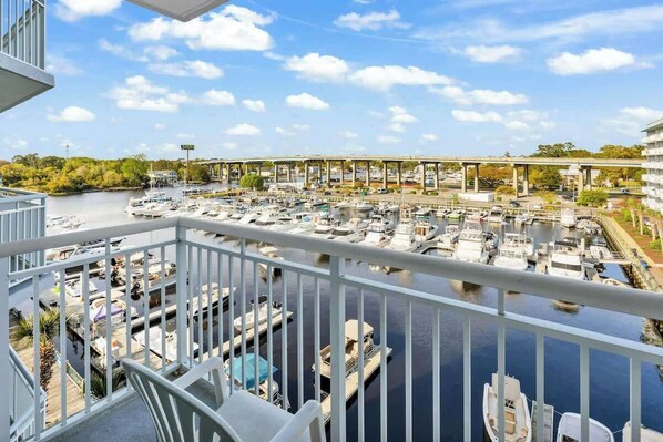 A marina with boats docked, a bridge in the background, and a balcony with a railing. - Harbourgate Unit 0404 (North Myrtle Beach)