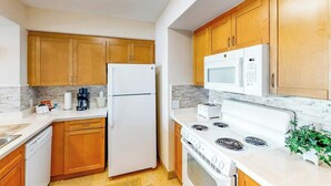A kitchen with wooden cabinets, a white refrigerator, a microwave, a stove, and a coffee maker. - Harbourgate Unit 0320 (North Myrtle Beach)
