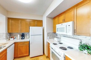 A kitchen with wooden cabinets, a white refrigerator, a microwave, a stove, and a coffee maker. - Harbourgate Unit 0320 (North Myrtle Beach)