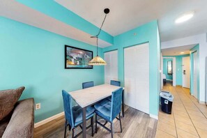 A room with teal walls, a dining table with chairs, a hanging lamp, and a framed picture on the wall. - Harbourgate Unit 0410 (North Myrtle Beach)