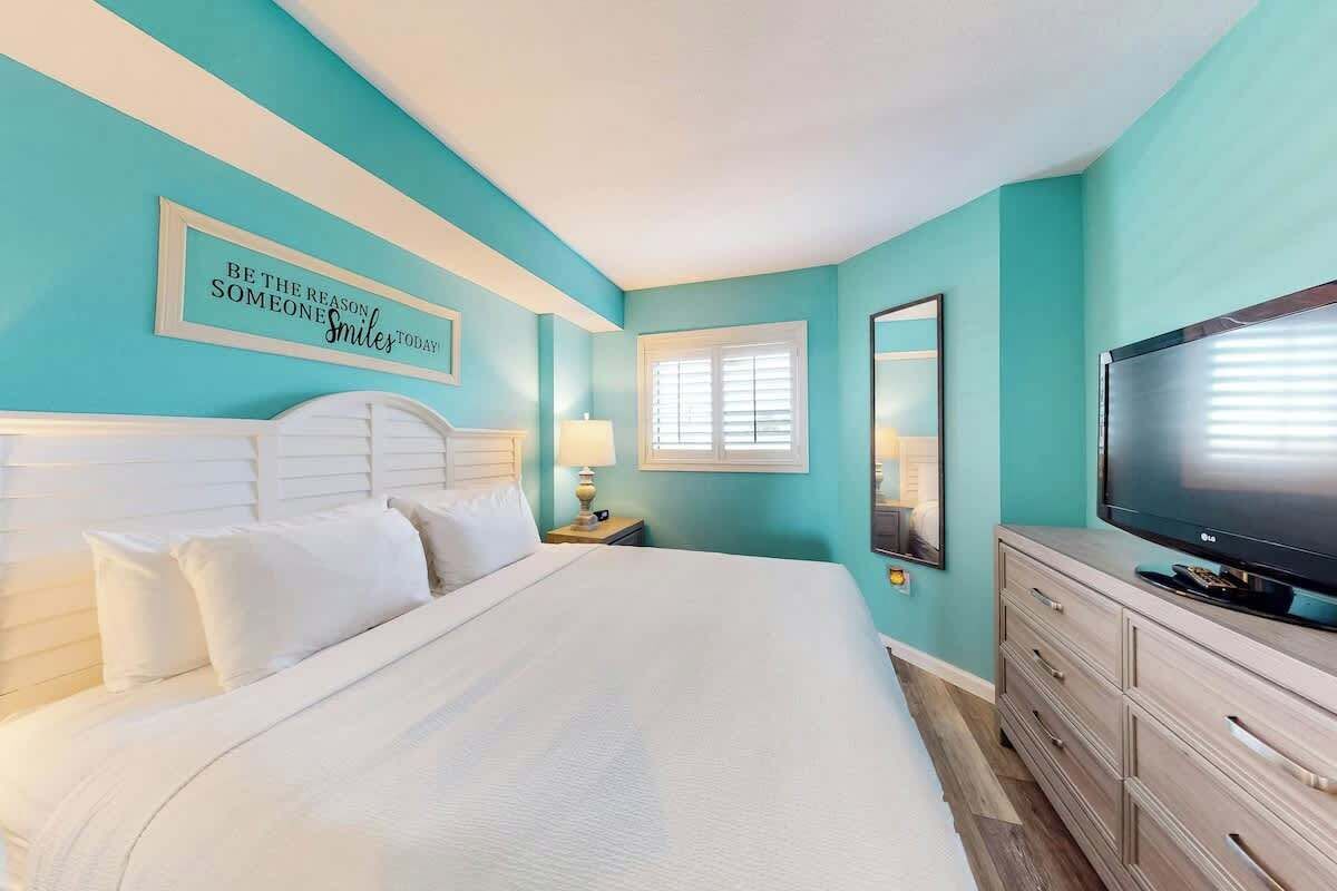 A hotel room with a large bed, a television, a dresser, and a wall with a motivational quote.