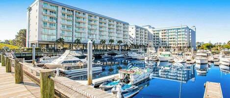 Un port de plaisance où sont amarrés de nombreux bateaux, une promenade en bois et un bâtiment d’hôtel à plusieurs étages doté de balcons.