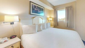 Quarto de hotel com cama grande, abajures, telefone e janela com cortinas.