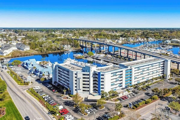 A multi-story hotel with a parking lot, a marina with boats, and a bridge in the background. - Harbourgate Unit 0405 (North Myrtle Beach)