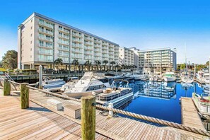 Ein Yachthafen mit mehreren vertäuten Booten, ein großes Hotelgebäude mit Balkonen und ein klarer, blauer Himmel.