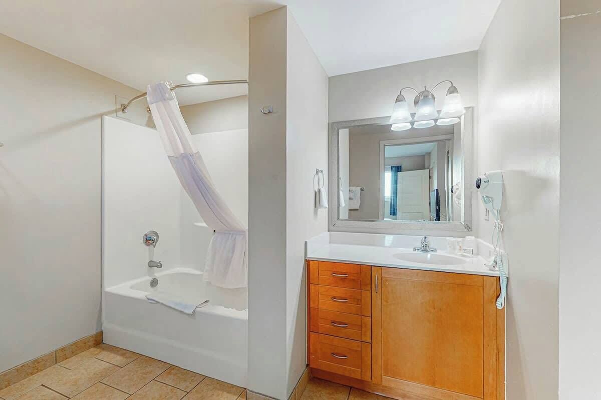 A bathroom with a bathtub, a vanity with a mirror, and a shower curtain.