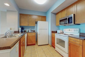 A kitchen with wooden cabinets, a white refrigerator, a microwave, a stove, and a sink. - Harbourgate Unit 0522 (North Myrtle Beach)