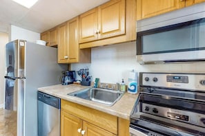 A kitchen with wooden cabinets, stainless steel appliances including a refrigerator, dishwasher, and oven, and a sink. - Ocean Park Resort 0322 (Myrtle Beach)