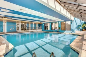 An indoor swimming pool with clear blue water, a tiled floor, and a view of the sky through the ceiling. - Ocean Park Resort 0322 (Myrtle Beach)