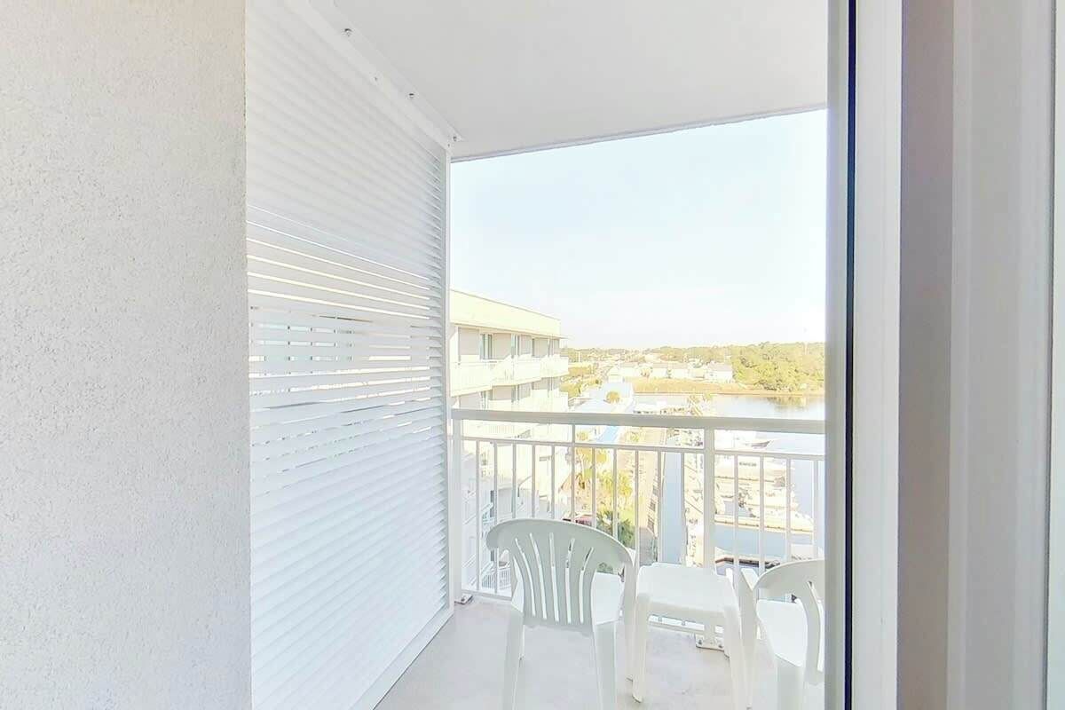 A balcony with white chairs and a view of a building and water.