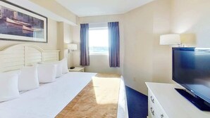 Ein Hotelzimmer mit einem Bett, einem Fernseher, einem Schreibtisch, einer Lampe und einem Fenster mit Vorhängen.