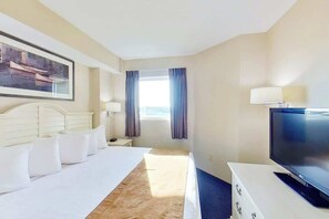 Ein Hotelzimmer mit einem Bett, einem Fernseher, einem Schreibtisch, einer Lampe und einem Fenster mit Vorhängen.