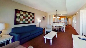 A living room with a blue sofa, a white coffee table, and a dining area with a table and chairs. - Harbourgate Unit 0626 (North Myrtle Beach)